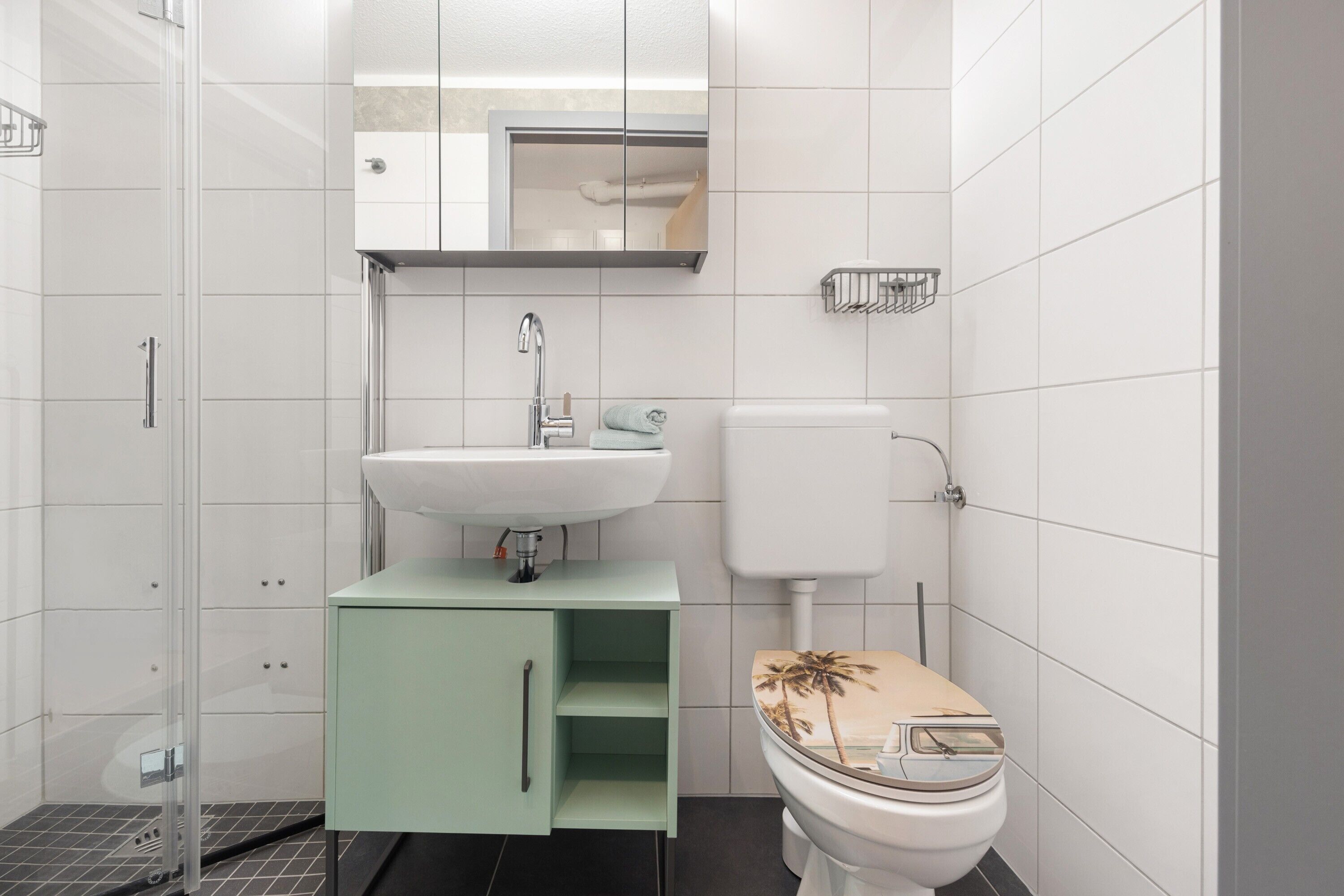 Een badkamer met een wit toilet, een wastafel, een spiegel en een douche.