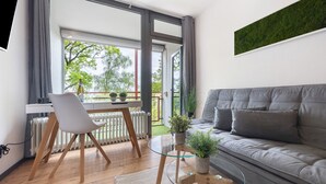 Un salon moderne avec un canapé gris, une table basse en verre, un fauteuil blanc et une vue sur la verdure à l’extérieur.