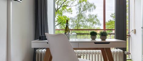 Ein modernes Zimmer mit einem weißen Schreibtisch, einem weißen Stuhl, einem Heizkörper und einem Fenster mit Blick auf Bäume.