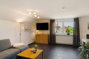 Ein Wohnzimmer mit einer Couch, einem Couchtisch, einem Fernseher, einem Schrank und einem Fenster mit Vorhängen.