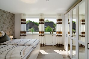 Een slaapkamer met een bed, een raam met gordijnen, een radiator en uitzicht op buiten.
