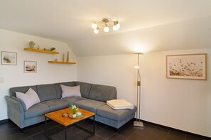 Ein Wohnzimmer mit grauem Sofa, einem Holztisch, einer Stehlampe und Wandregalen.