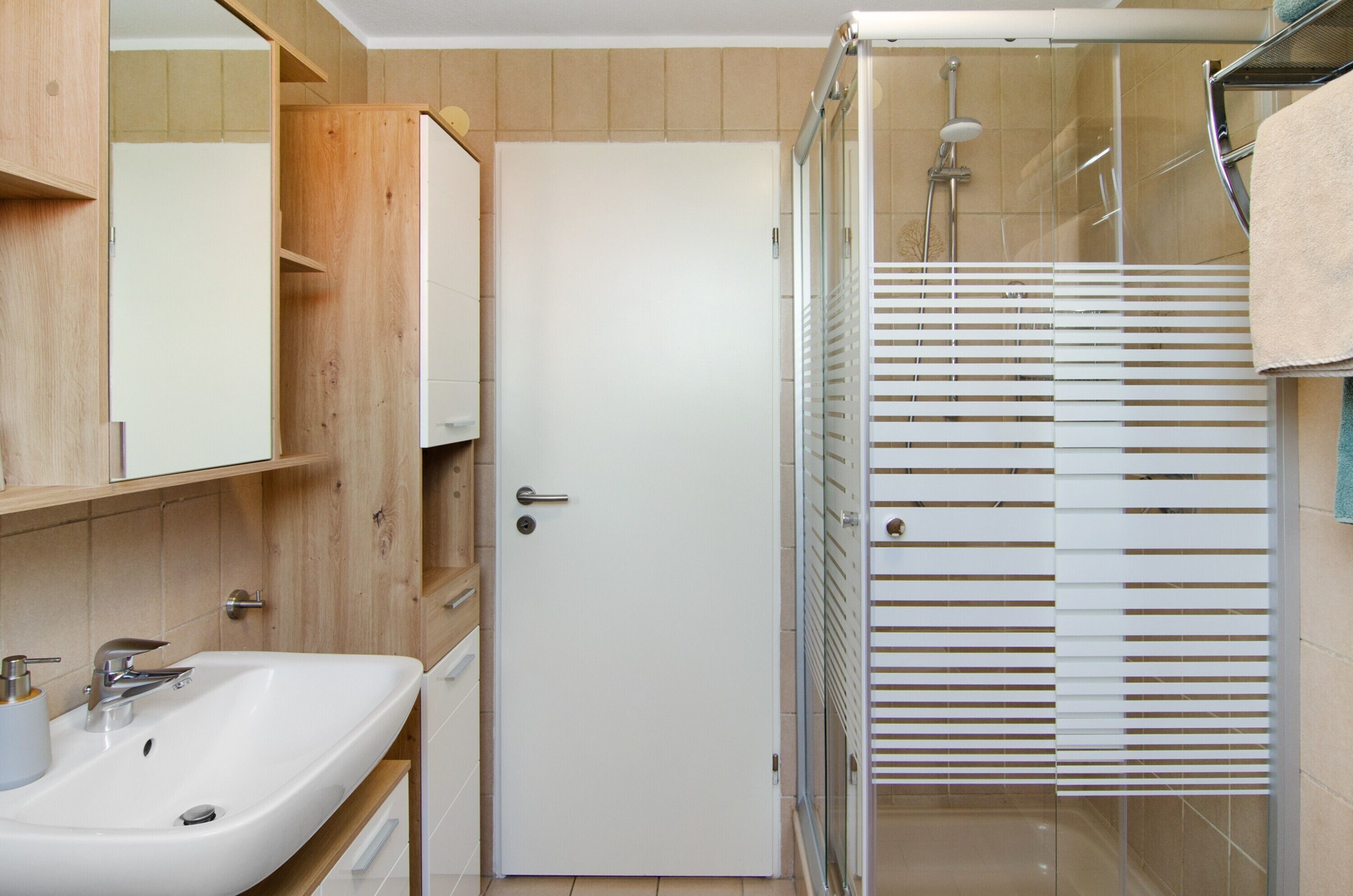 Ein Badezimmer mit Waschbecken, Spiegel, Holzausstattung, einer Dusche mit Glastür und einem Handtuch an der Wand.