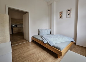 A bedroom with a wooden bed, a small kitchenette, and a door leading to another room.