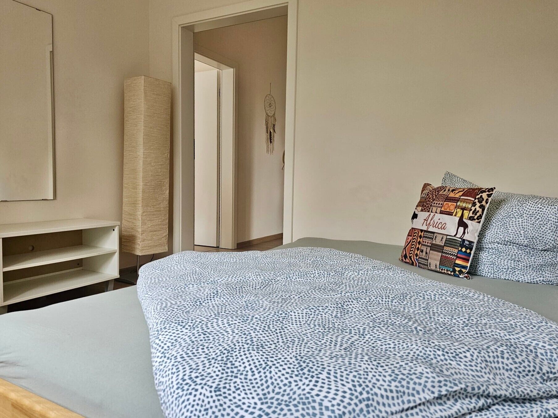 Un dormitori amb llit, armari, mirall i una porta que dona a una altra habitació.