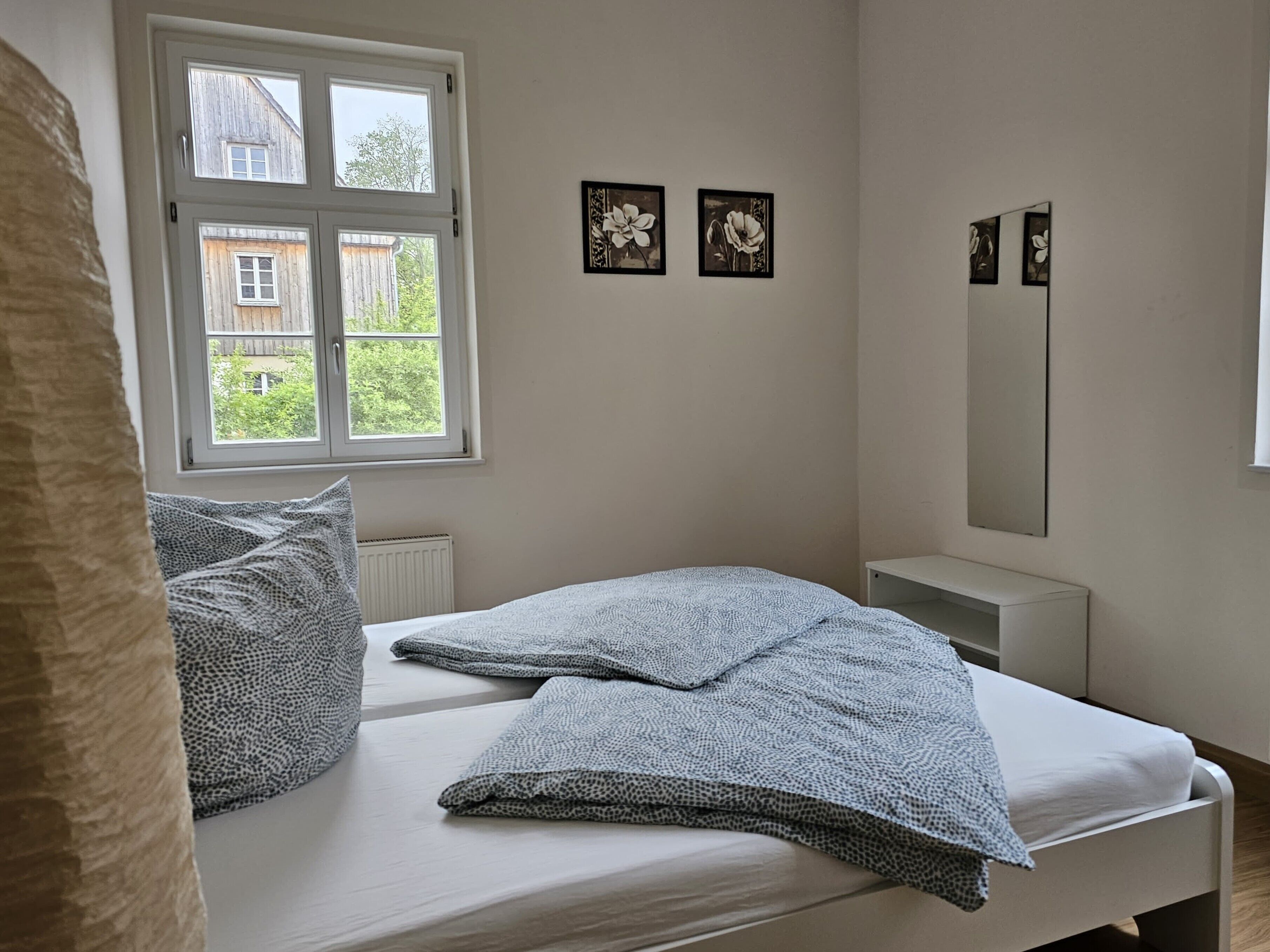 A bedroom with a bed, a window, a radiator, and wall-mounted artwork.