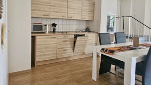Een moderne keuken met houten kastjes, een magnetron, en een eethoek met een witte tafel en zwarte stoelen.