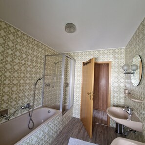 A bathroom with a shower, a sink, a mirror, and a wooden door.