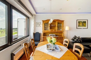 Uma sala de jantar com uma mesa de madeira, cadeiras, um vaso com flores e vista pela janela.