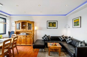 Sala de estar com sofá de couro preto, armário de madeira e área de jantar com cadeiras e mesa.