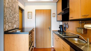 A compact kitchen with a stone accent wall, wooden cabinets, a black countertop, and a built-in oven. - Apartment 'Ferienwohnung Dünenblick' with Sea View, Balcony and Wi-Fi (Wangerland)