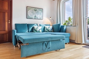 Un canapé turquoise avec une fonction convertible en lit, une carte du monde accrochée au mur, une fenêtre avec des rideaux et un radiateur.