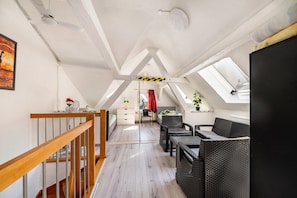 Une pièce mansardée spacieuse avec un escalier en bois, un coin repas avec des meubles en osier, un lit et une grande fenêtre.