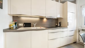Une cuisine moderne avec des meubles blancs, un évier en acier inoxydable et un plan de travail noir.