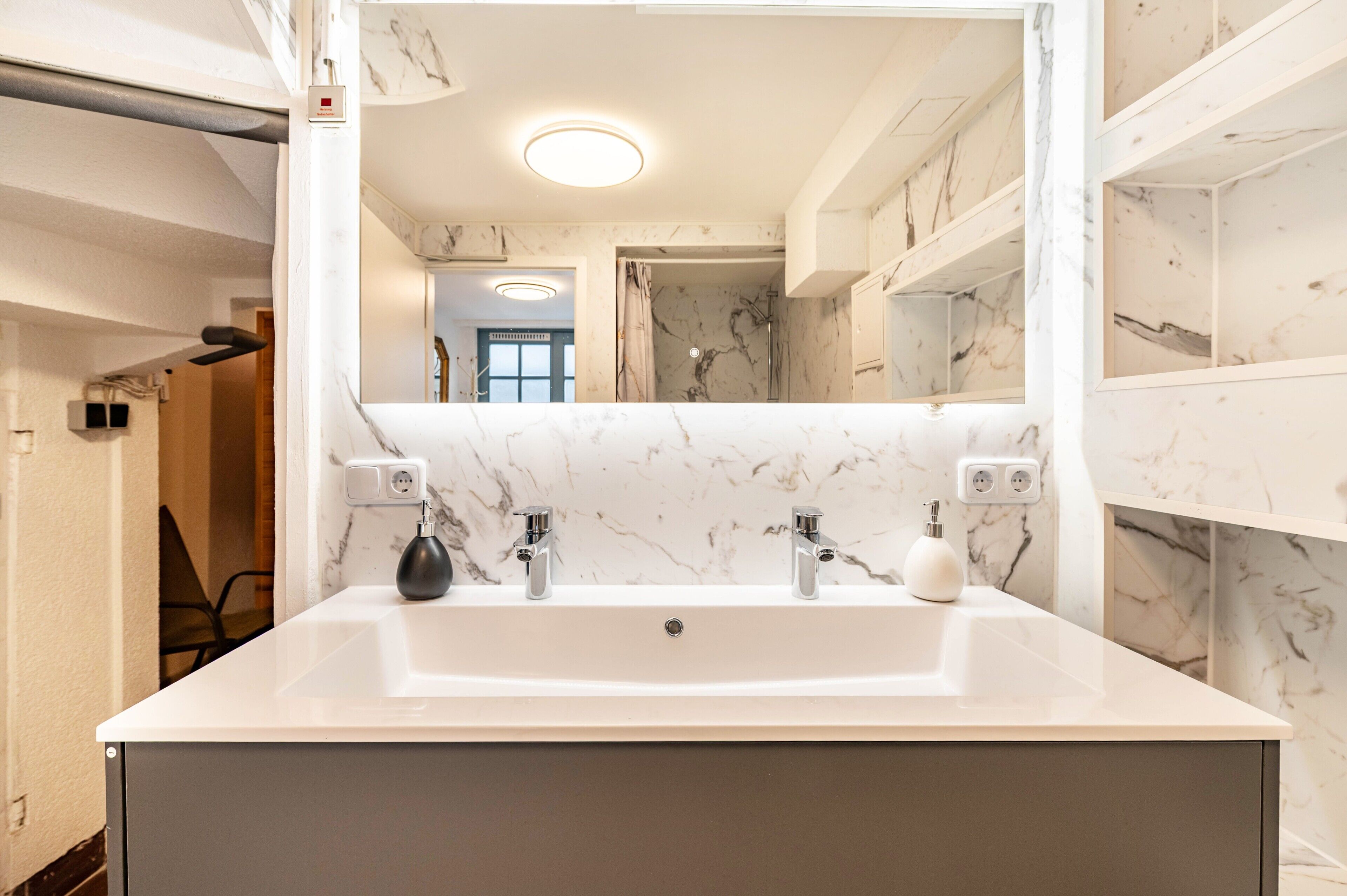 A bathroom with a white marble sink, two faucets, and a mirror.