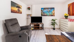 Un salon avec un canapé, un téléviseur posé sur un meuble en bois, une plante en pot et des œuvres d’art accrochées aux murs.