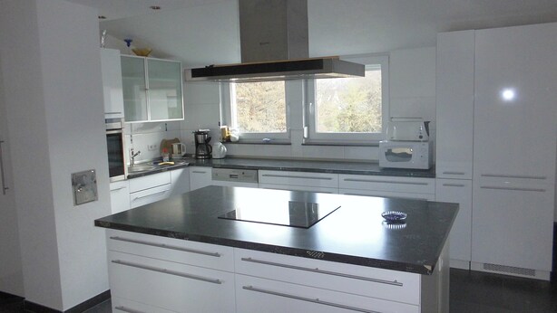 A modern kitchen with white cabinets, a large island with a black countertop, and a window above the sink. - Apartment 'Stuifenblick' with Mountain View, Private Garden and Wi-Fi (Waldstetten)