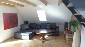 A modern living room with a sectional sofa, a round coffee table, a painting, and a skylight.
