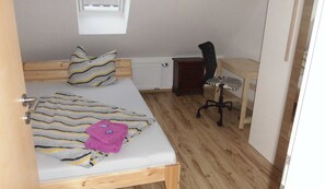 A small, neatly arranged bedroom with a bed, a desk, a chair, and a radiator.