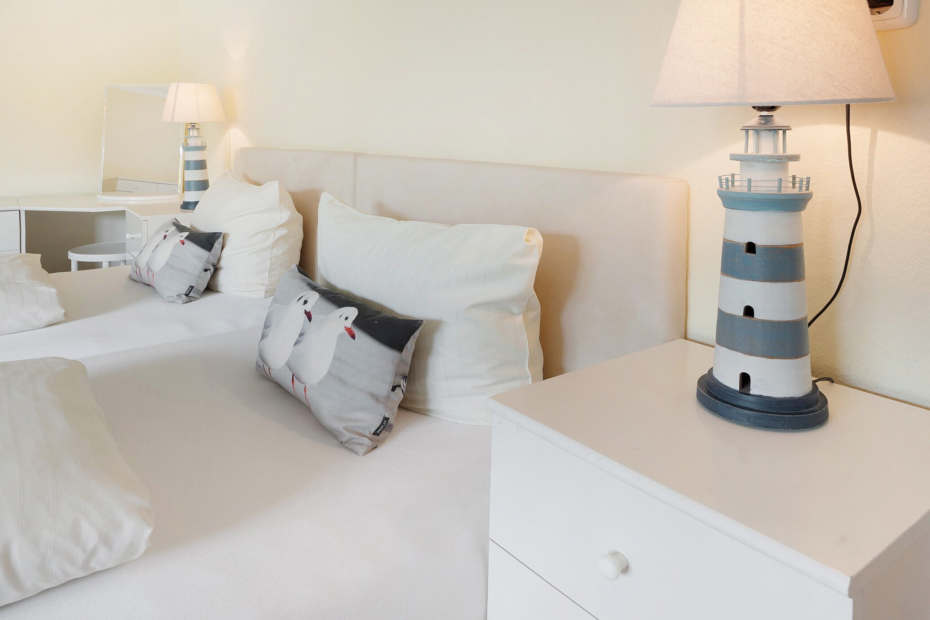 Ein Hotelzimmer mit einem Bett, Kissen, einem Nachttisch, einer Lampe und einer dekorativen Leuchtturm-Lampe.