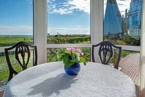 A room with a table, chairs, a vase with flowers, and a view of greenery and buildings.