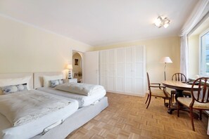 A bedroom with two beds, a dining table with chairs, a lamp, and a wardrobe.
