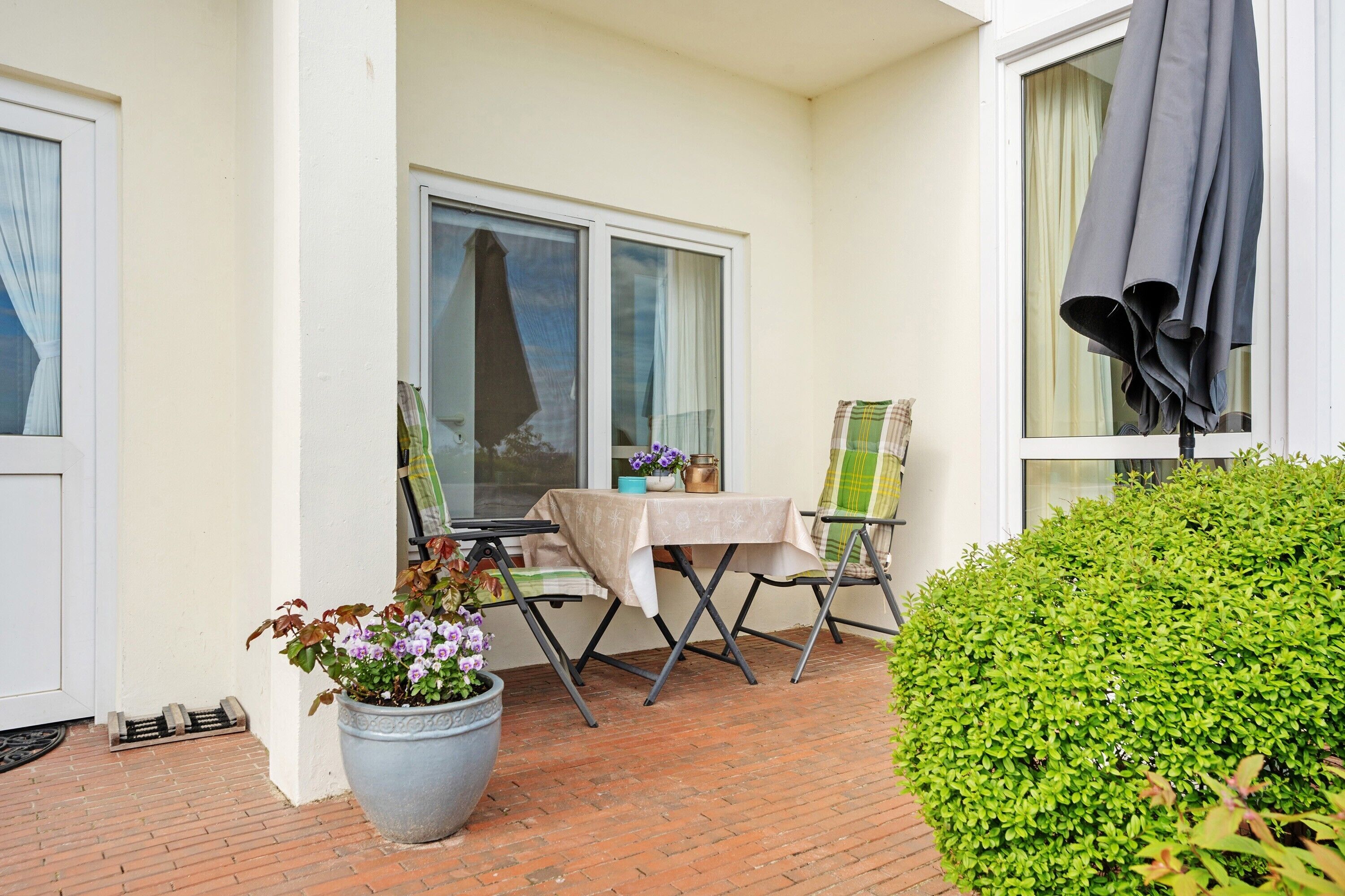 Eine Terrasse mit Tisch, Stühlen, einem Topfpflanzen und einem Hecken.