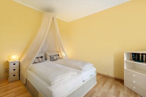 A bedroom with a canopy bed, bedside drawers, a bedside lamp, a wicker storage unit, and a bookshelf. - Apartment 'Wohnung 2' with Private Terrace, Shared Garden and Wi-Fi (Hohwacht (Ostsee))