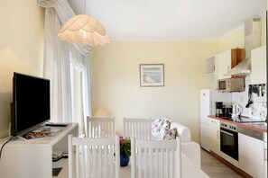 A modern living room with a flat-screen TV, white furniture, a dining table, and a kitchen area with appliances. - Apartment 'Wohnung 2' with Private Terrace, Shared Garden and Wi-Fi (Hohwacht (Ostsee))