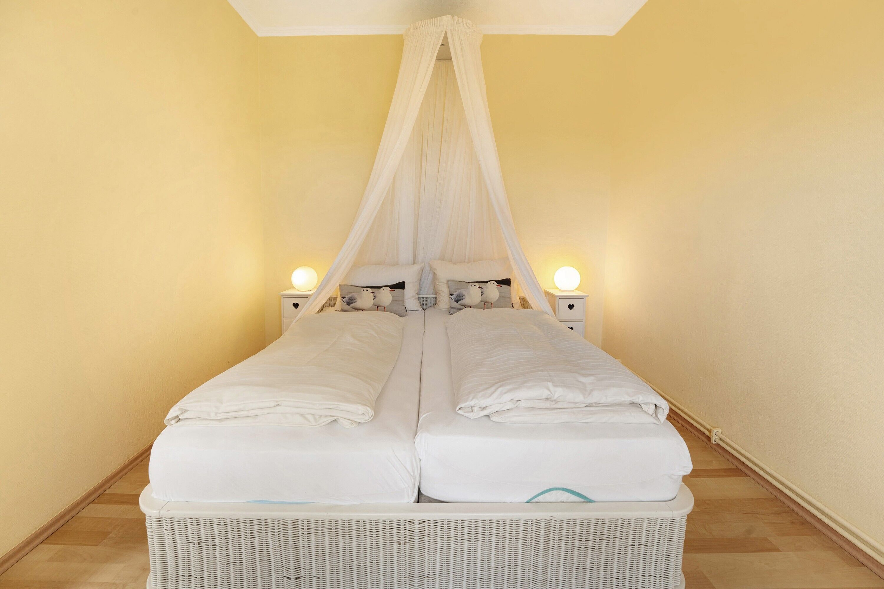 Ein Bett mit Baldachin, Nachttische und einem Korpus aus Rattan.