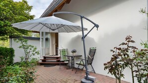 Eine Terrasse mit Tisch, Stühlen und Sonnenschirm, sowie ein kleiner Gartenbereich.
