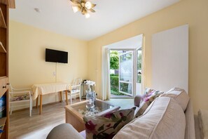 Un salon comprenant un canapé, une table avec un vase, un téléviseur à écran plat et un coin repas avec des chaises et une table.