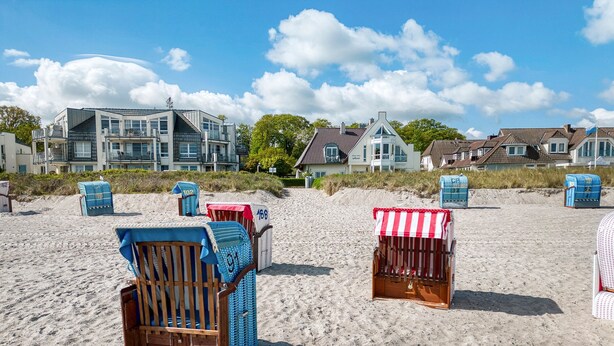 Strandkörbe und eine Strandhütte an einem Sandstrand, im Hintergrund Häuser.
