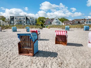 Des chaises de plage et un abri de plage sur une plage de sable, avec des maisons en arrière-plan.