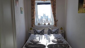 Un dormitorio con una cama, dos mesitas de noche, una ventana con cortinas y vistas a árboles y montañas.
