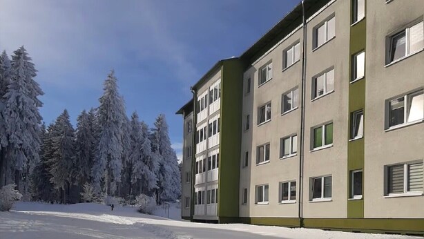 Un edificio de varios pisos con techo plano y ventanas amplias, rodeado de árboles cubiertos de nieve.