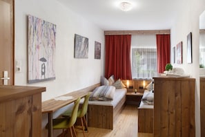 A cozy room with a wooden desk, a bench, and a bed with red curtains. There are framed artworks on the wall and a small table with a lamp. - Apartment 'Ferienwohnung Waldzauber' with Sea View, Shared Terrace and Wi-Fi (Oetz)