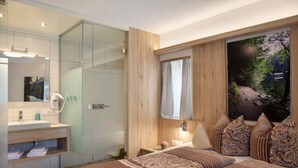 Une chambre à coucher moderne avec un grand lit, une salle de bain dotée d’une douche à parois de verre, et une vue sur une forêt par la fenêtre.