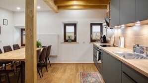 Une cuisine moderne avec des poutres en bois, un coin repas avec une table et des chaises, et une petite fenêtre agrémentée d’une plante.