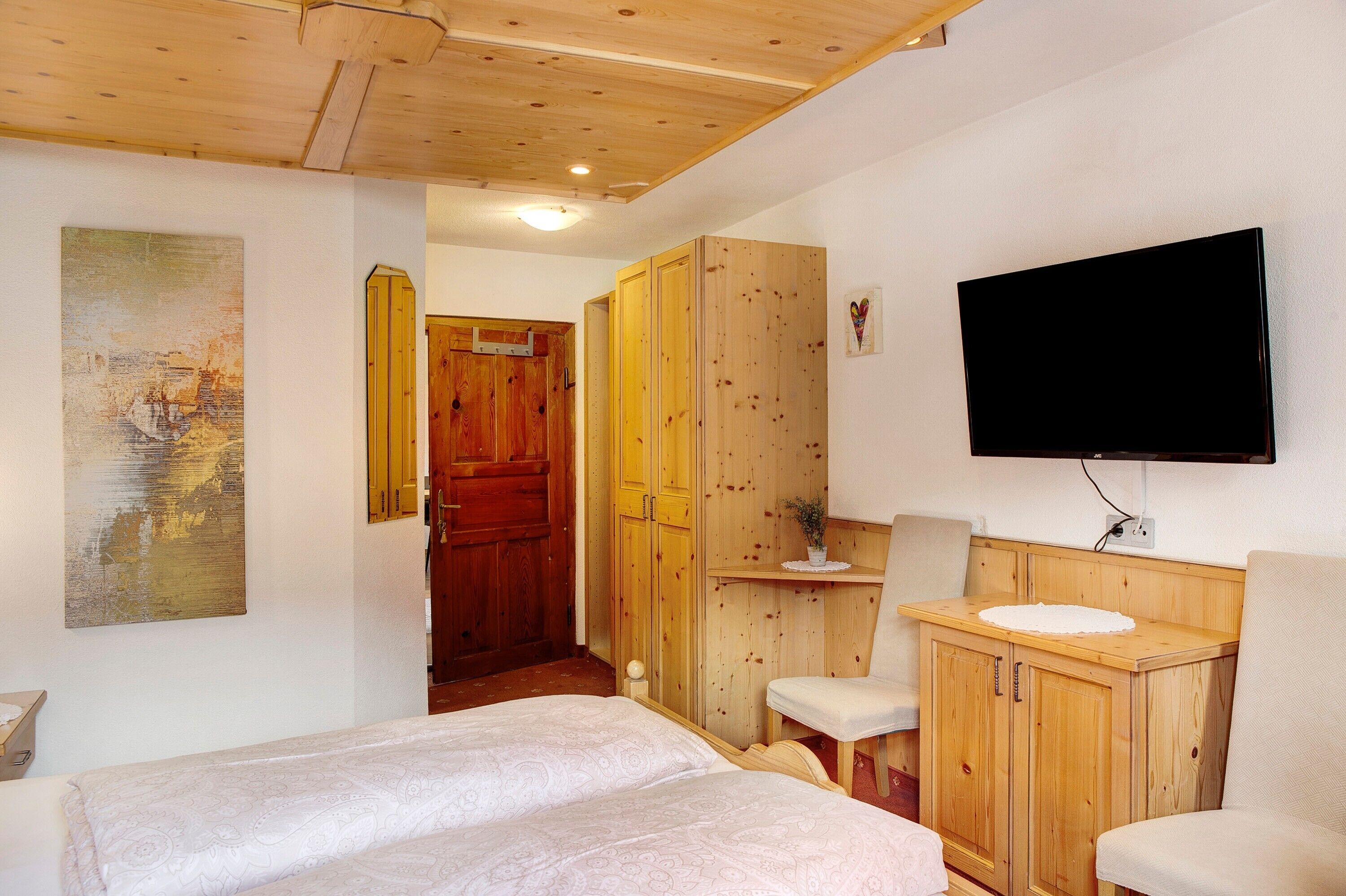 A room with a bed, a TV mounted on the wall, wooden furniture, and a painting on the wall.