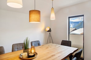 A dining area with a wooden table, chairs, pendant lights, a floor lamp, and a window with a mountain view. - Apartment 'Ferienwohnung Sonnenschein' with Sea View, Shared Terrace and Wi-Fi (Oetz)