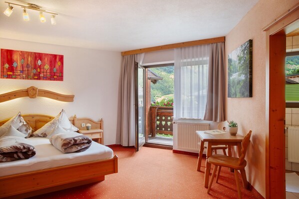 Un dormitorio con cama, escritorio, silla, ventana con cortinas, radiador y un cuadro en la pared.