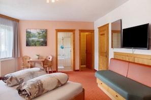 A hotel room with a bed, a sofa, a TV, a desk with a chair, and a bathroom door.