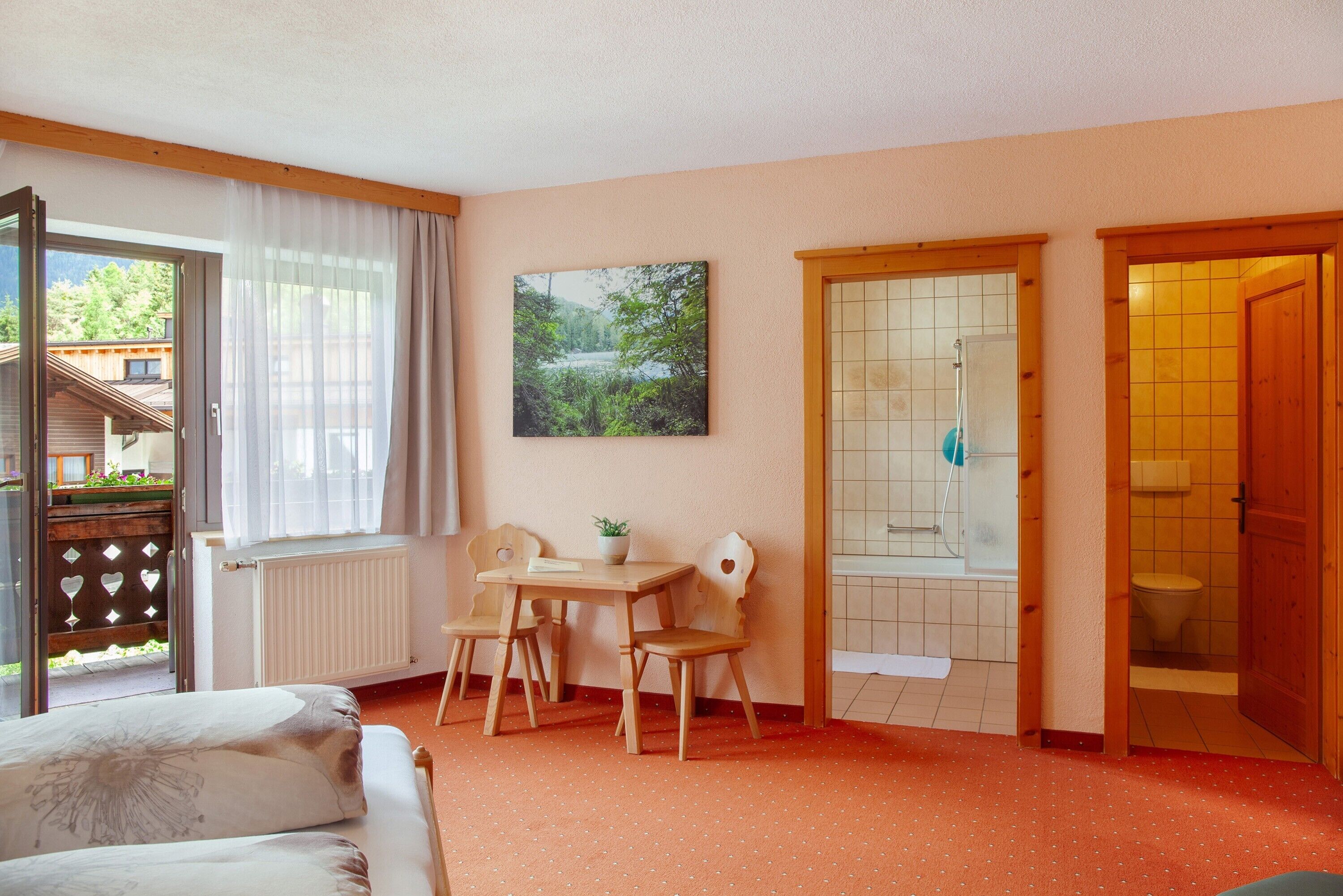 Une pièce comprenant un lit, une table avec des chaises, une fenêtre avec des rideaux, un tableau et une porte de salle de bain.
