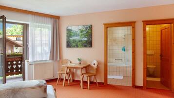 Une pièce comprenant un lit, une table avec des chaises, une fenêtre avec des rideaux, un tableau et une porte de salle de bain.