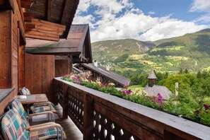 Un balcón de madera con vistas a un valle, una mesa de madera con sillas y un arreglo floral.