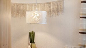 Et værelse med et træbord, en vægophængt makramevævning, en hængende lysarmatur og en potteplante.