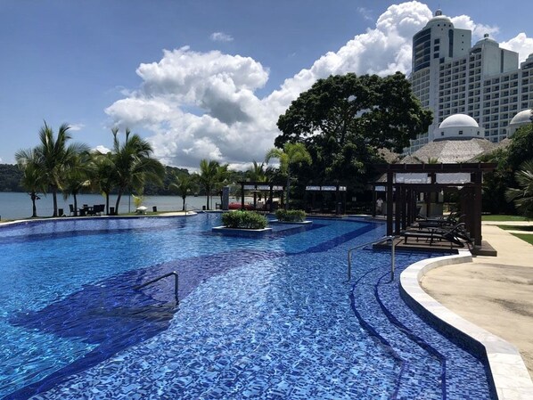 Relax by the resort pool surrounded by palm trees and a gazebo.