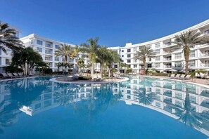 A hotel with a large pool surrounded by palm trees and lounge chairs.