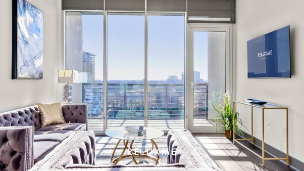 Un salon moderne doté d’une grande porte-fenêtre coulissante donnant sur un balcon, d’un canapé capitonné, d’une table basse en verre et d’un style de décoration minimaliste.